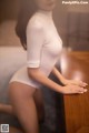 A woman in a white bodysuit leaning on a table.