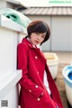 A woman in a red coat leaning against a wall.