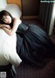 A woman in a black dress laying on a bed.