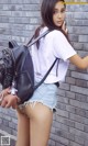 A woman in shorts and a white shirt holding a black backpack.