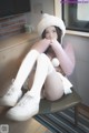 A woman sitting on a chair wearing white stockings and a pink sweater.