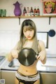 A woman in lingerie holding a frying pan in a kitchen.