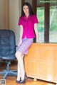 A woman in a pink shirt and skirt sitting on a desk.