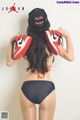 A woman in a black bikini and a black hat holding a pair of shoes.